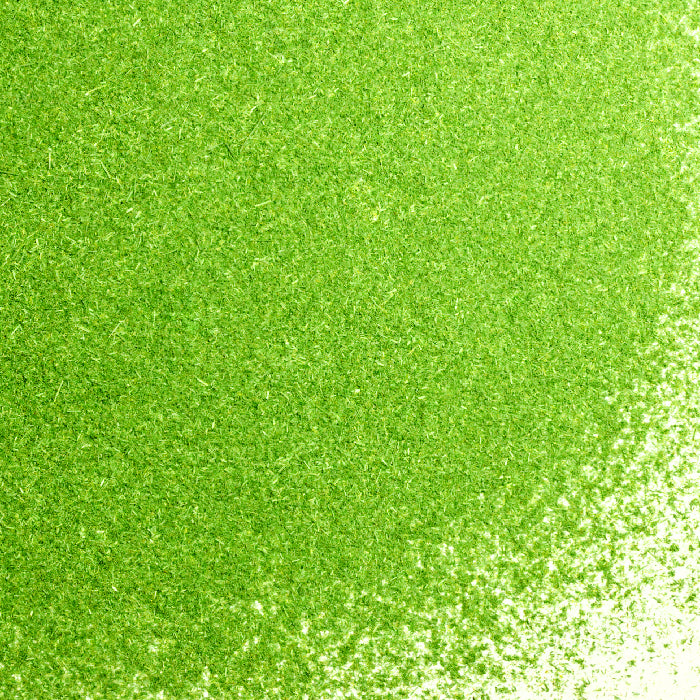 A close-up of Whole Spice Inc. Lemon Grass Powder shows a green, textured surface similar to finely shredded lemon grass, with a gradient density that becomes lighter toward the bottom right corner.