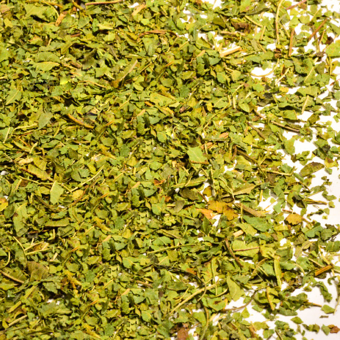 Close-up of Whole Spice Inc. Lemon Verbena Leaves—small, flat pieces in varying green and yellow shades spread over a white surface; a natural option for relieving indigestion.