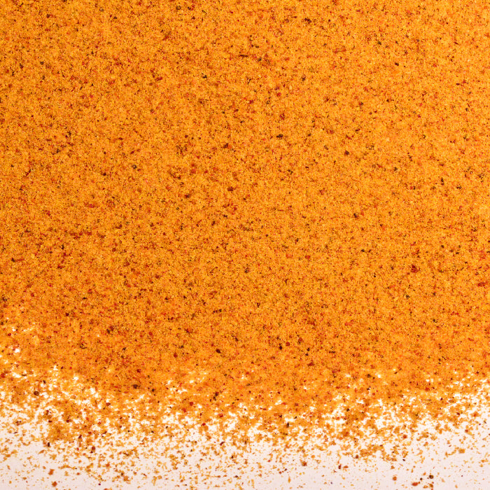 A close-up of finely and coarsely ground Mace Powder by Whole Spice Inc. is shown scattered on a white background, showcasing this vibrant nutmeg alternative.