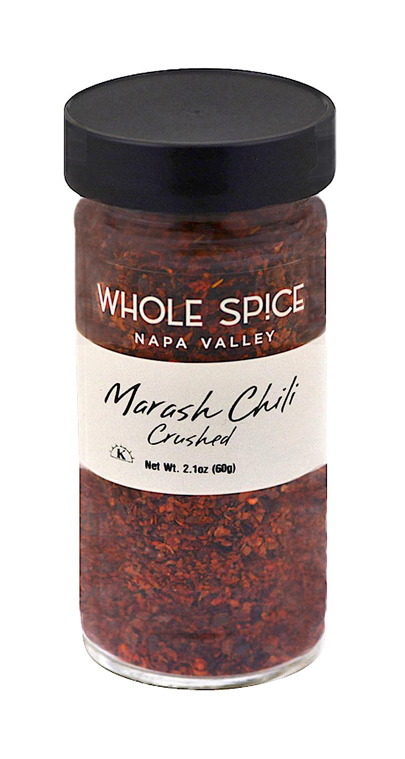 A clear spice jar from Whole Spice Inc. labeled Marash Chili Crushed, filled with vibrant red pepper flakes popular in Middle Eastern dishes, topped with a black lid. Net weight: 2.1 oz (60g).
