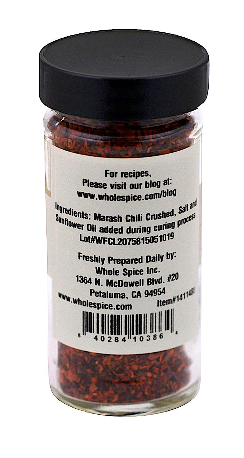 A clear jar labeled on the back holds Marash Chili Crushed by Whole Spice Inc., a Middle Eastern staple with chili, salt, and sunflower oil. The label details ingredients, preparation, and Whole Spice Inc. contact info.