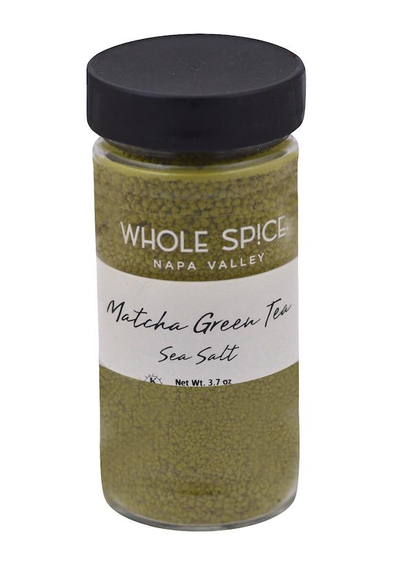 A clear spice jar with a black lid from Whole Spice Inc., labeled Matcha Green Tea Sea Salt, contains green gourmet salt blended with premium matcha. Net weight: 3.7 oz.