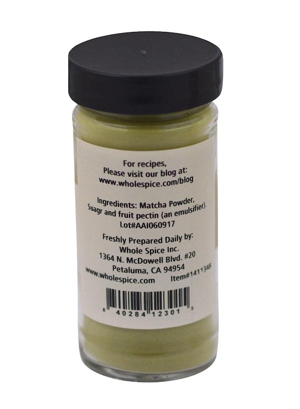 A small glass jar with a black lid holds Matcha Pre-Mix by Whole Spice Inc. The label shows ingredients, prep details, a website for Matcha drink recipes, and the Whole Spice Inc. company address.
