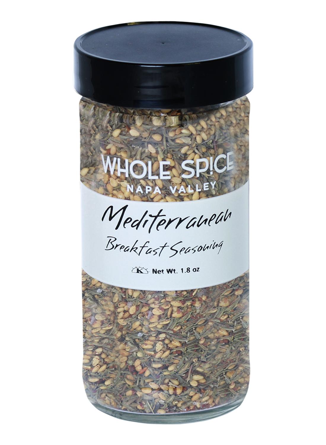 A clear spice jar with a black lid from Whole Spice Inc. labeled Mediterranean Breakfast Seasoning, containing a blend of dried herbs, sesame seeds, and spices. Net weight: 1.8 oz.