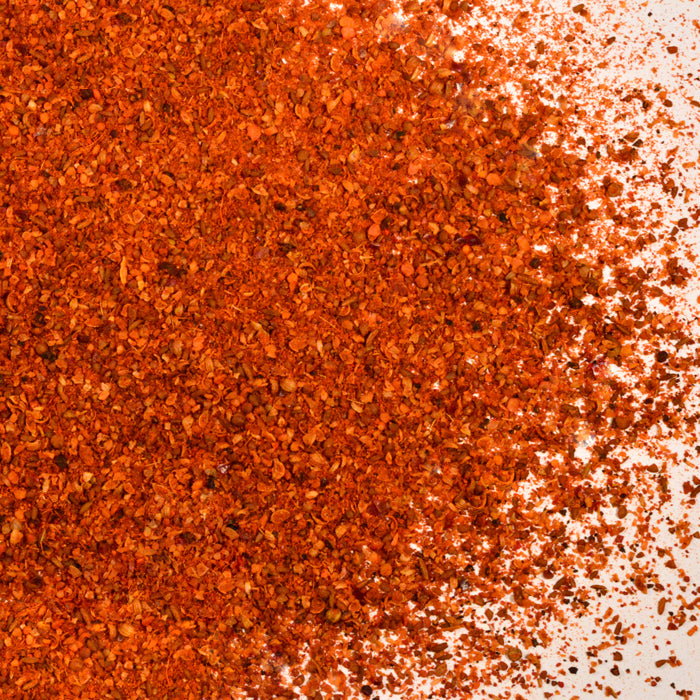 Whole Spice Inc.’s Moroccan Lamb Melange, a finely ground spice blend, is scattered on a white surface—densely packed on the left, with sparser granules trailing to the right.