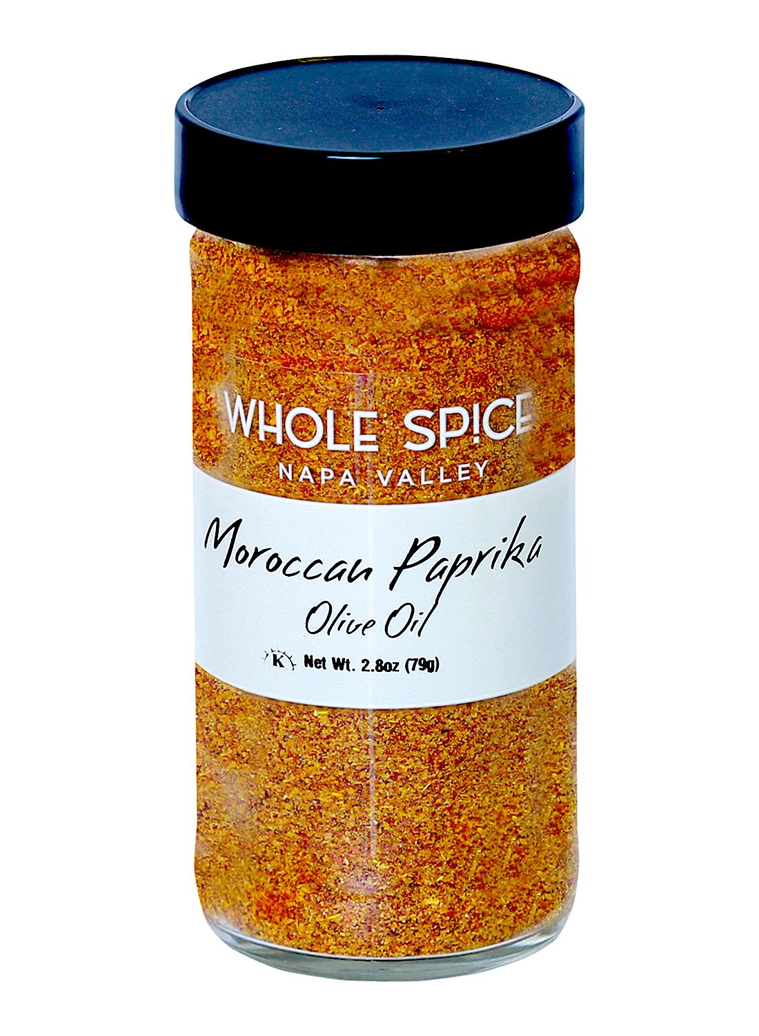 A clear glass jar with a black lid holds Whole Spice Inc.’s Moroccan Paprika & Olive Oil blend. The white label displays black handwritten-style text showing the product name and weight (2.8 oz/79g).