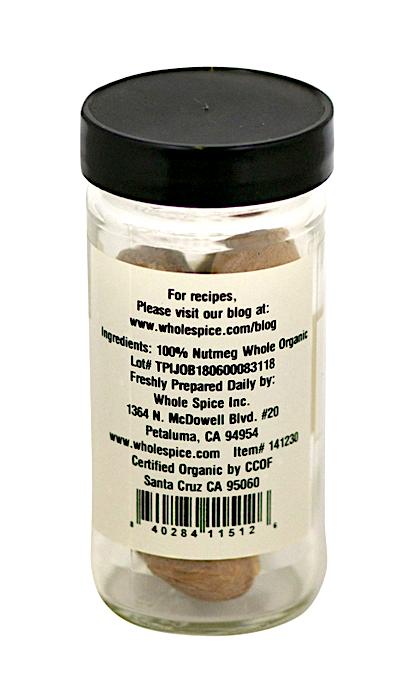 A clear glass jar with a black lid contains Whole Spice Inc. Nutmeg Whole Organic. The label displays ingredients, address, certifications, and a recipe website. Whole nutmeg is visible inside—ideal for sweet or savory dishes.