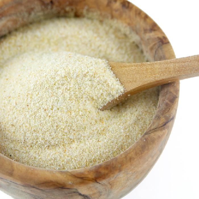 A wooden bowl holds Whole Spice Inc. Onion Granulated Organic, fine off-white dehydrated onion powder, with a wooden spoon scooping some.