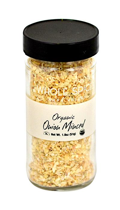 A clear glass jar with a black lid contains minced organic onion spice from Whole Spice Inc., labeled Onion Minced Organic, Net Wt. 1.8 oz (51g).