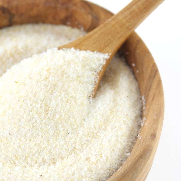 A wooden bowl filled with Whole Spice Inc. Onion Powder Organic and a wooden spoon scooping some, featuring a hint of natural anti-caking agent to keep it smooth and fresh.