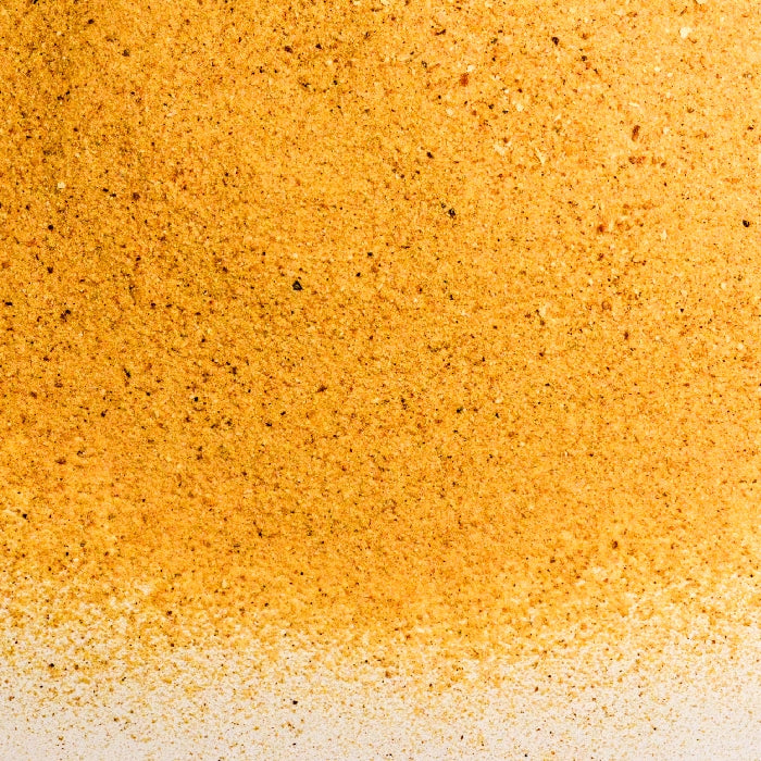A close-up view of Whole Spice Inc. Orange Peel Powder—a fine orange-brown powder—scattered unevenly across a white surface.