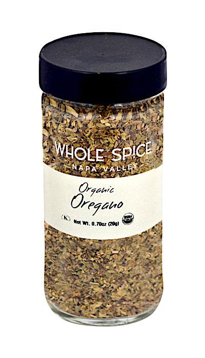A clear glass jar with a black lid contains Whole Spice Inc. Oregano Organic dried oregano leaves. The label shows a net weight of 0.7 oz (20g).