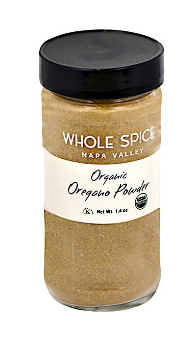 A glass jar of Whole Spice Inc. Oregano Powder Organic with a black lid contains light brown, dried oregano powder, an aromatic Mediterranean herb. The jar has a net weight of 1.4 oz and bears the USDA organic seal.