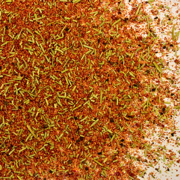 A close-up of Whole Spice Inc. Roasted Chicken Blend Organic, featuring red, orange, and green organic spices plus French gray salt scattered on a white surface.