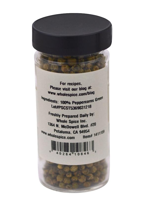 A clear jar with a black lid contains Peppercorns Green by Whole Spice Inc., filled with 100% green peppercorns. The label lists the sole ingredient and includes the manufacturer's details and website.