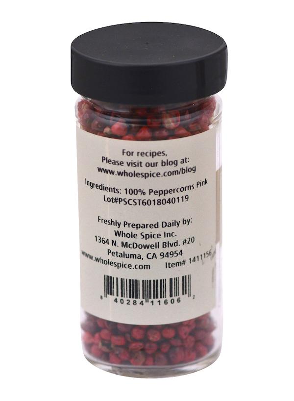A clear jar labeled Peppercorns Pink from Whole Spice Inc., Petaluma, CA, contains 100% pink peppercorns. The label includes company info, a barcode, and a website offering peppercorn recipes.