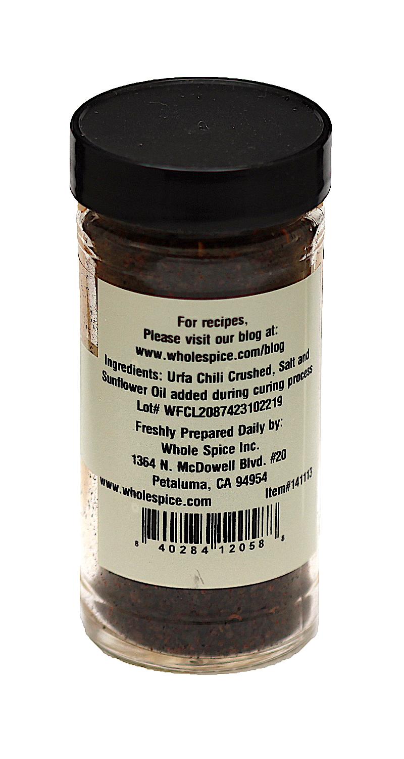 A clear jar labeled "Urfa Chili Crushed" by Whole Spice Inc. shows ingredients—Urfa chili (Turkish chili), salt, sunflower oil—the brand’s Petaluma, California address, company info, and a barcode on a white label.