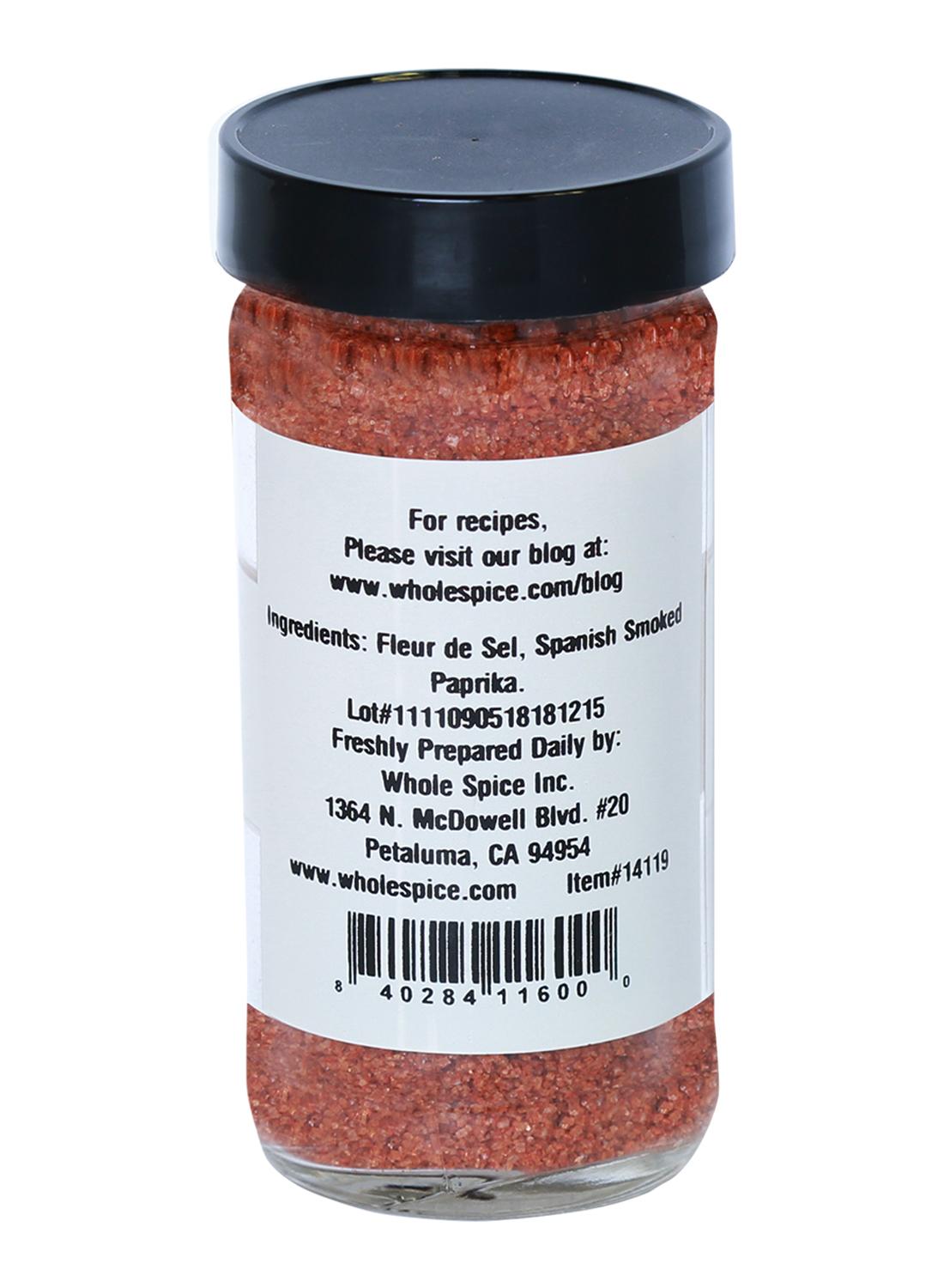 A clear spice jar with a black lid holds reddish Pimenton Salt by Whole Spice Inc.; the label lists ingredients, company info, address, and a barcode.