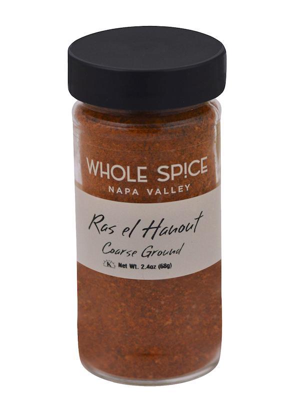 A clear glass jar with a black lid labeled “Whole Spice Inc. Ras el Hanout Coarse Ground, Net Wt. 2.4oz (68g),” filled with reddish-brown Moroccan spice blend.