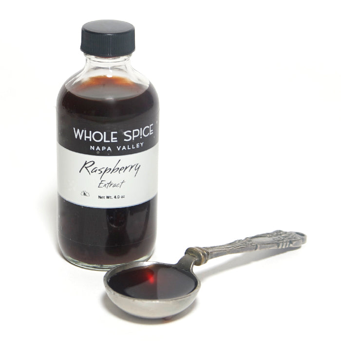 A 4-ounce bottle of Whole Spice Inc. Raspberry Extract sits beside an ornate silver spoon filled with dark liquid, offering natural raspberry flavor ideal for desserts and adding fruity notes to your recipes.