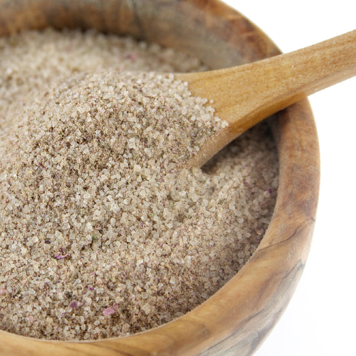 A wooden bowl holds Whole Spice Inc. Rose Sugar, a coarse gourmet blend with light and dark specks. A wooden spoon scoops the visually striking sugar mix, perfect for adding elegance to your dishes.