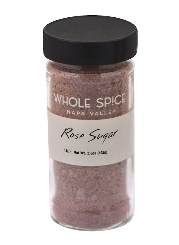 A clear glass jar with a black lid holds pink Rose Sugar by Whole Spice Inc., featuring a white label and Net Wt. 3.6oz (102g)—a delightful addition to your gourmet sugar collection.
