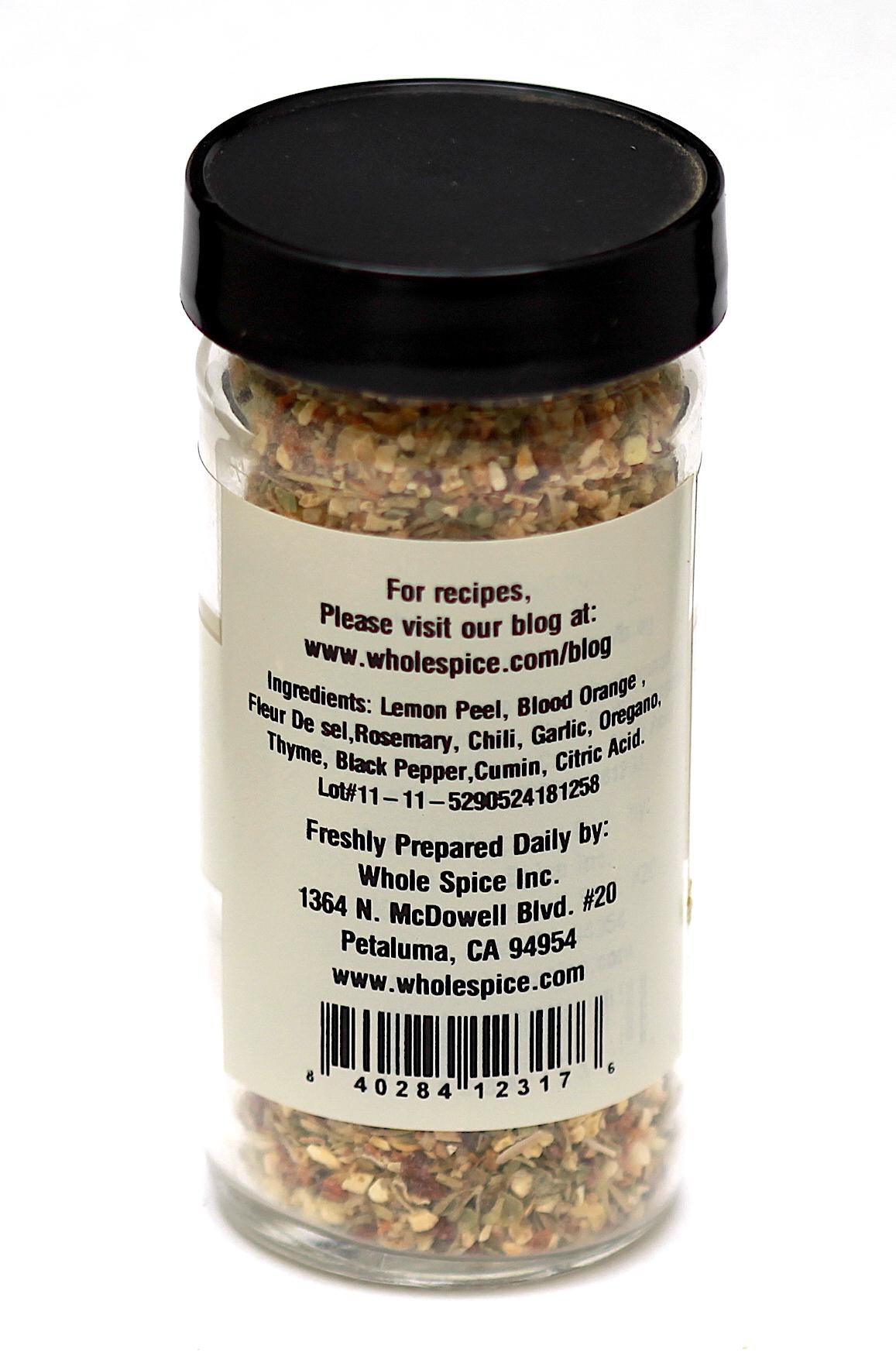 A clear spice jar of Whole Spice Inc.’s Rosemary Green Olives Seasoning features a black lid and label with ingredients like lemon peel, rosemary, chili, garlic, and oregano. Ideal for pairing with green olives. The jar stands upright on a white background.