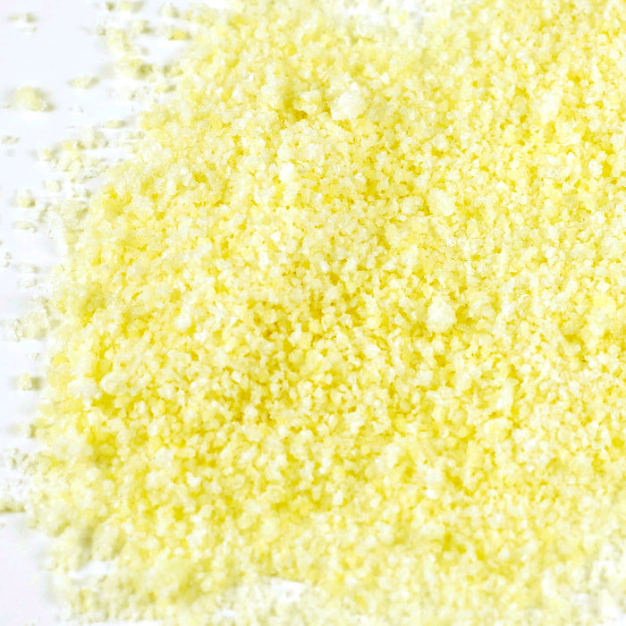 A close-up of Whole Spice Inc. Lime Salt, finely ground and pale yellow, spread on a white surface, offering a burst of citrus flavor.