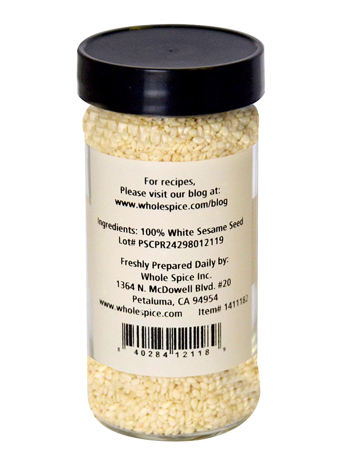 A clear glass jar of Whole Spice Inc. Sesame Seeds White Hulled with a black lid. Back label has ingredients, company info, address, barcode, and recipe website. Filled with premium sesame seeds.