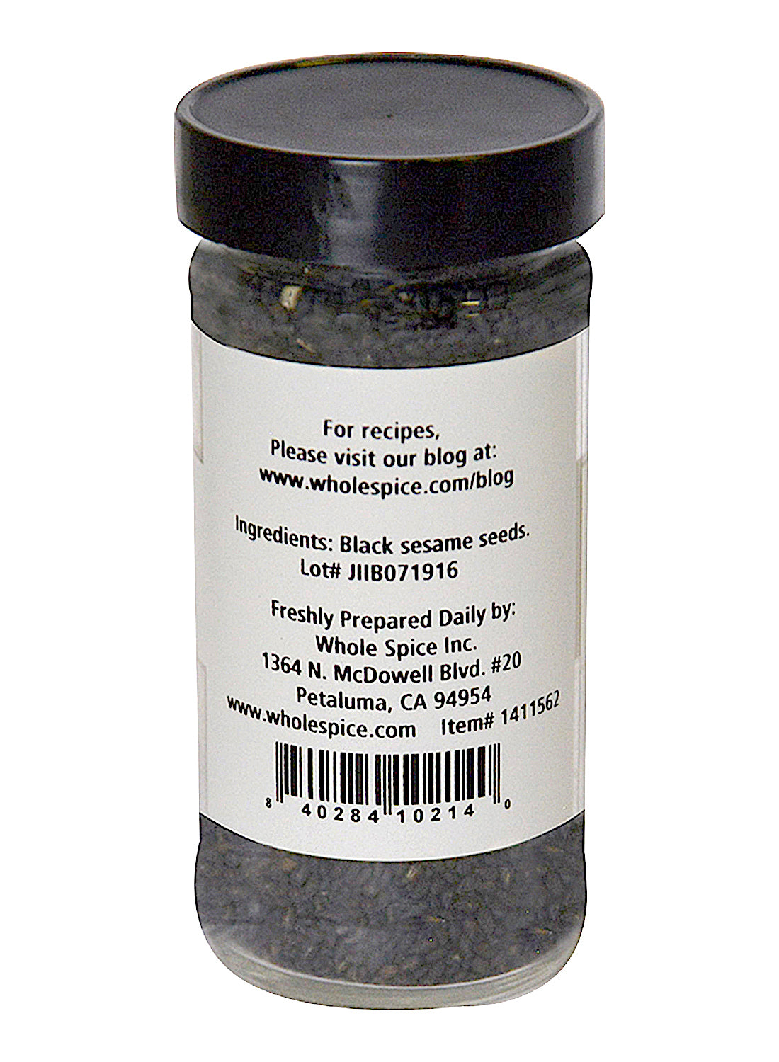 A clear spice jar with a black lid holds Whole Spice Inc.’s Sesame Seeds Black Toasted. The label includes ingredients, lot number, preparation details, company info, and a barcode. The jar is from Petaluma, California.