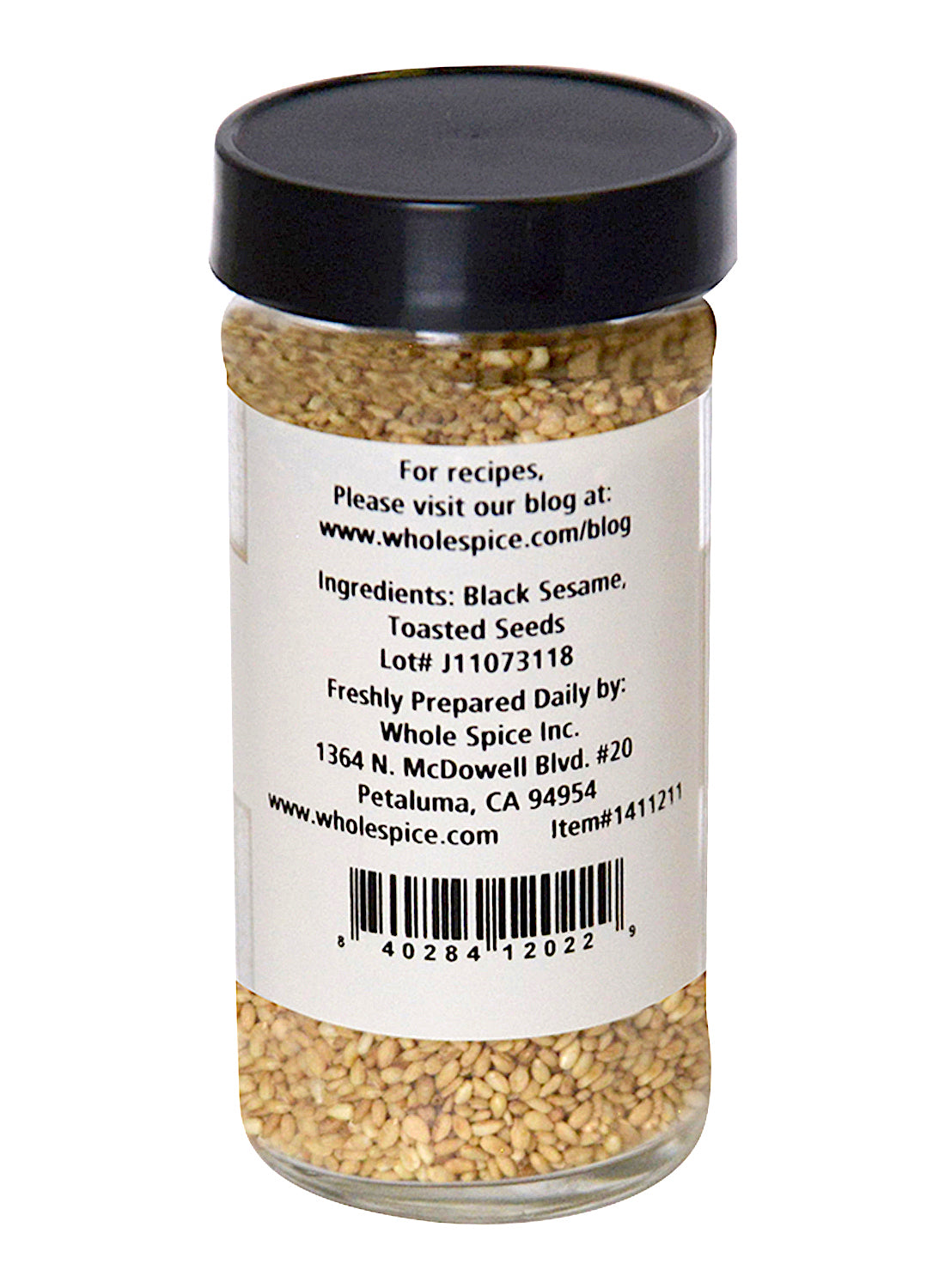 A clear spice jar with a black lid contains Sesame Seeds Natural Toasted by Whole Spice Inc., featuring unhulled toasted sesame seeds. The label lists ingredients, company info, and a website for recipes.