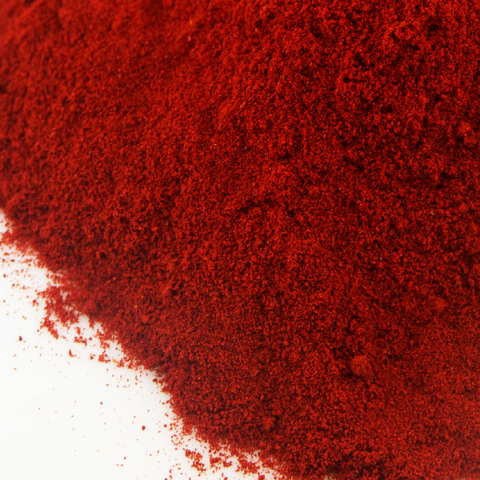 A close-up of vibrant red, finely ground Sweet Smoked Paprika by Whole Spice Inc. spread across a white surface.