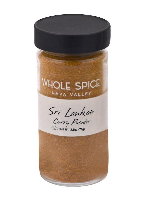 A clear spice jar with a black lid labeled Whole Spice Inc. Sri Lankan Curry Powder holds golden-brown curry spices, ideal for rice and curry dishes. Net weight: 2.5oz (71g).