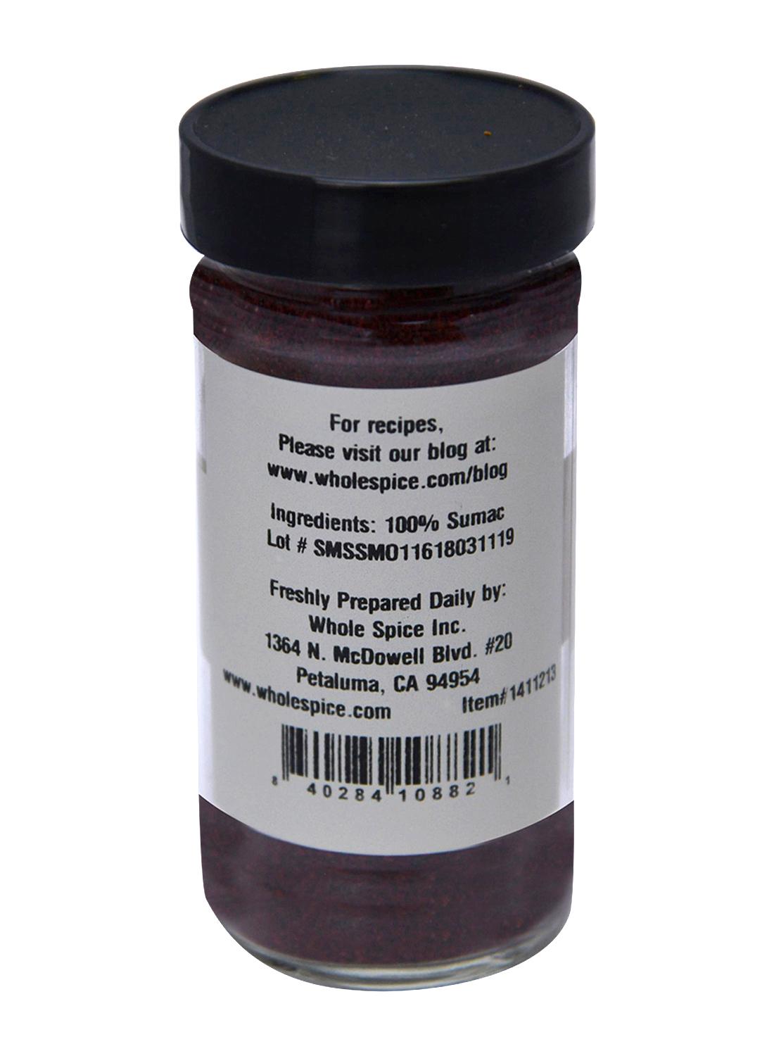 A glass spice jar with a black lid labeled "Sumac Ground" by Whole Spice Inc. contains 100% sumac spice. The label includes the manufacturer's info, lot number, and a website for recipes.