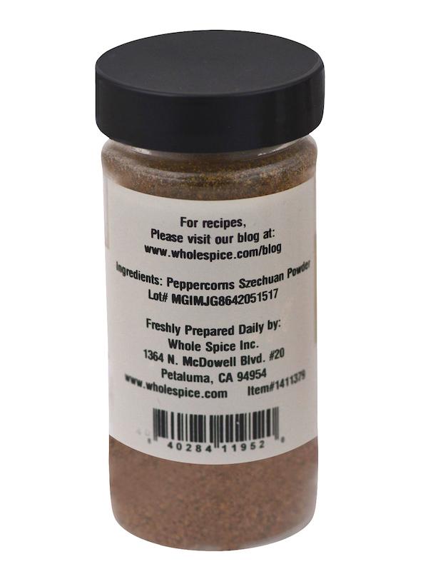 A clear jar with a black lid holds Whole Spice Inc.'s Peppercorns Szechuan Powdered, a brown spice. The label lists Szechuan pepper as an ingredient, suggests it for poultry, and displays a website, address, and barcode.