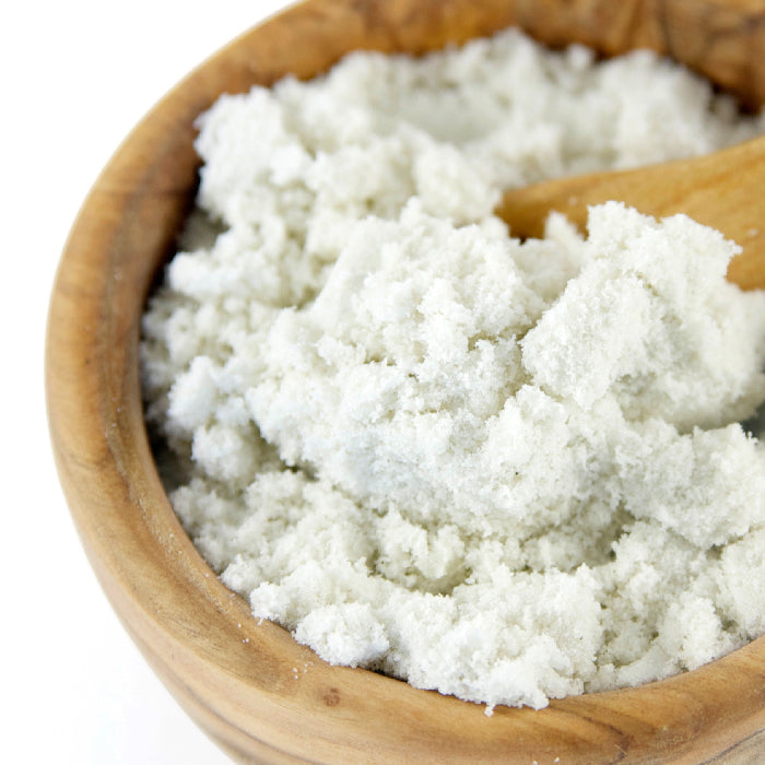 A close-up of Velvet de Guerande Sea Salt by Whole Spice Inc., showing fine, white crystals in a wooden bowl with a wooden spoon scooping the delicate, unrefined finishing salt.