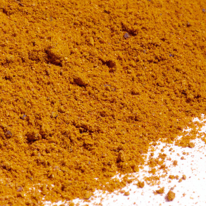 A close-up of orange-brown Vindaloo Curry Powder by Whole Spice Inc., scattered on a white surface—perfect for adding authentic flavor to Indian curry dishes.
