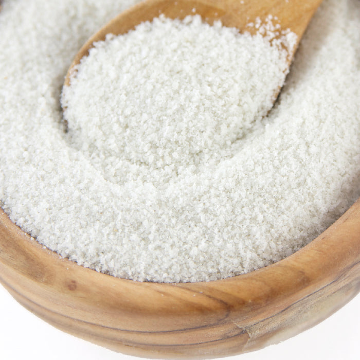 A close-up of Whole Spice Inc. White Truffle Sea Salt—coarse gourmet seasoning in a wooden bowl, with a wooden spoon inside scooping some salt.