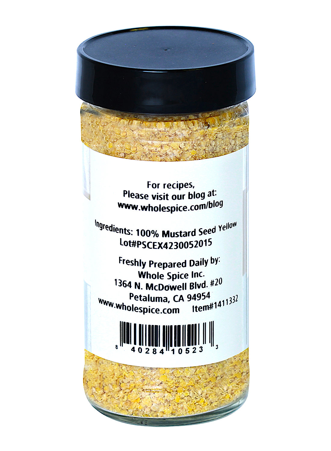 A clear spice jar with a black lid holds Whole Spice Inc. Yellow Mustard Seed Coarse Ground. The label features ingredients, company info, and recipe website. A barcode appears at the bottom of the label.