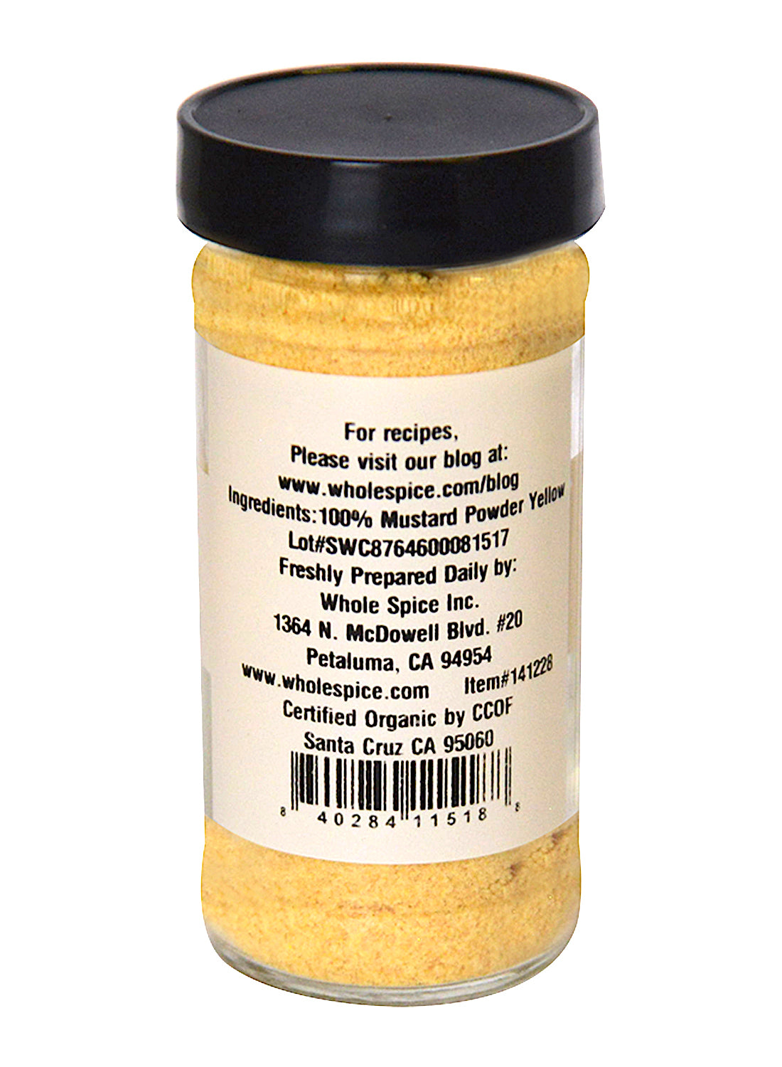 A clear glass jar with a black lid contains Whole Spice Inc. Yellow Mustard Seed Ground Organic. The back label shows the ingredients, company details, website, organic certification, and barcode.