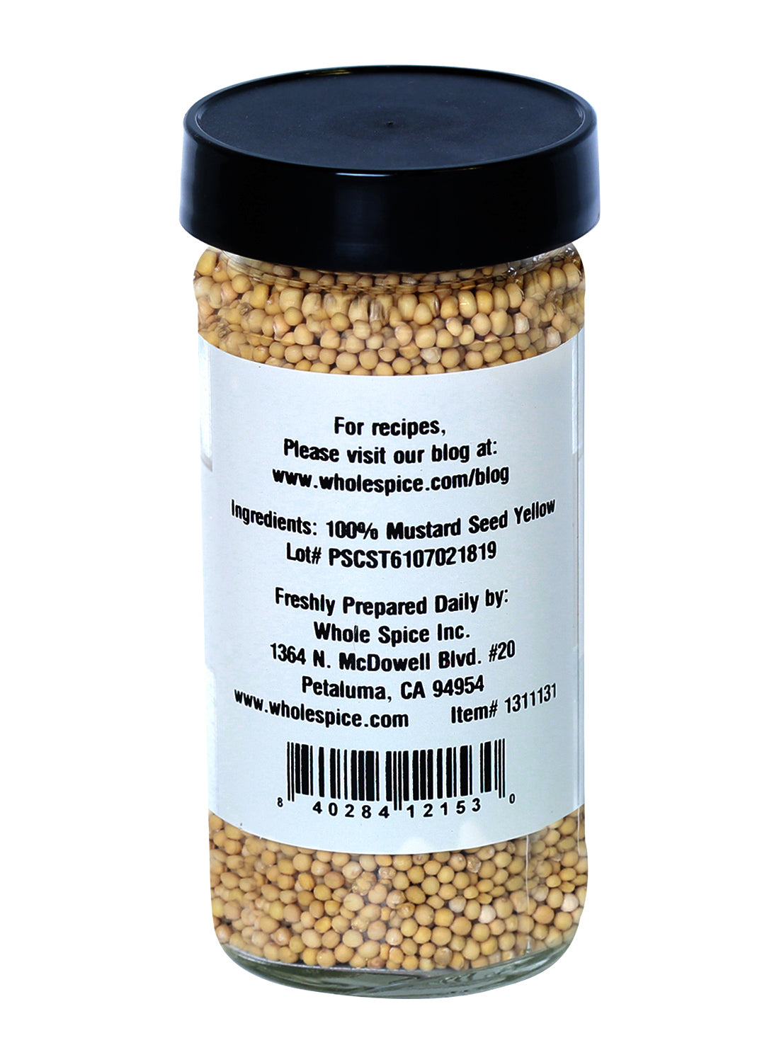 A clear glass jar with a black lid contains Whole Spice Inc. Yellow Mustard Seed Whole—100% yellow mustard seed, ideal for barbecue sauces or salad dressings. The back label has the brand info, address, and recipe website.